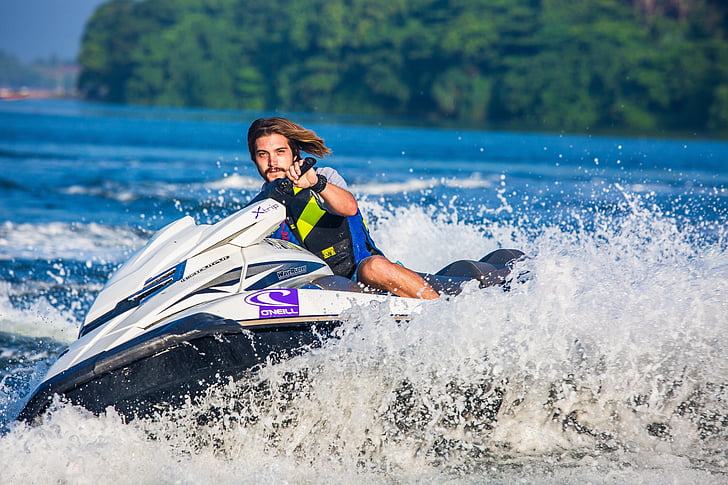 A man rides a jet ski across a vibrant blue lake, creating splashes of water and enjoying a sunny day.