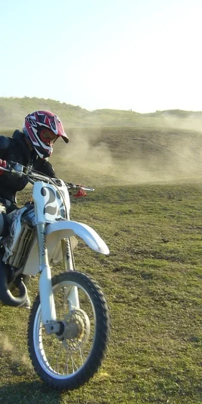 A motocross rider in protective gear kicks up dust while making a sharp turn on a grassy track.